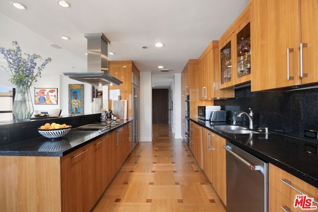 kitchen with stainless steel appliances, dark stone countertops, tasteful backsplash, sink, and island range hood