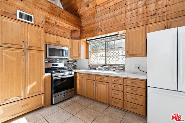 kitchen featuring high vaulted ceiling, light tile patterned floors, appliances with stainless steel finishes, and tile counters