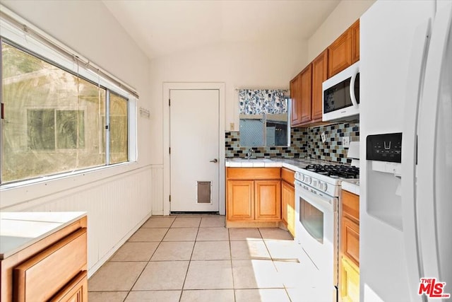 kitchen with white appliances, light tile patterned floors, sink, backsplash, and lofted ceiling