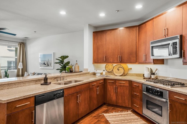 kitchen with light stone countertops, sink, kitchen peninsula, stainless steel appliances, and dark hardwood / wood-style floors