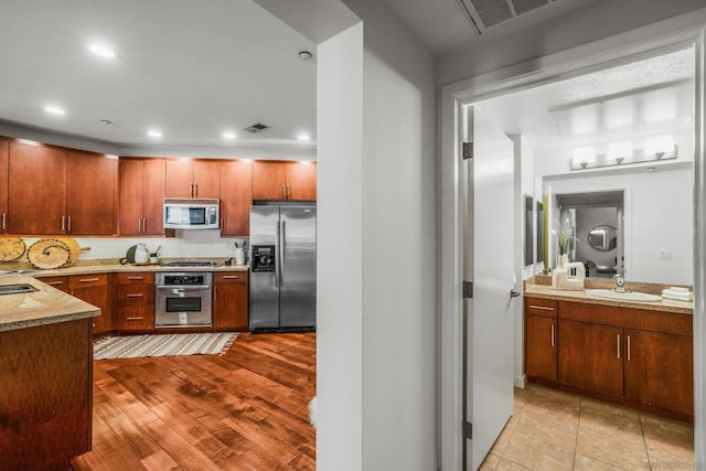 kitchen with light stone counters, sink, stainless steel appliances, and light hardwood / wood-style floors