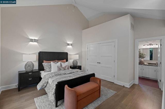 bedroom with wood-type flooring, a closet, ensuite bath, and lofted ceiling