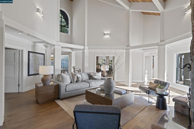 living room featuring decorative columns, a high ceiling, hardwood / wood-style flooring, and beam ceiling