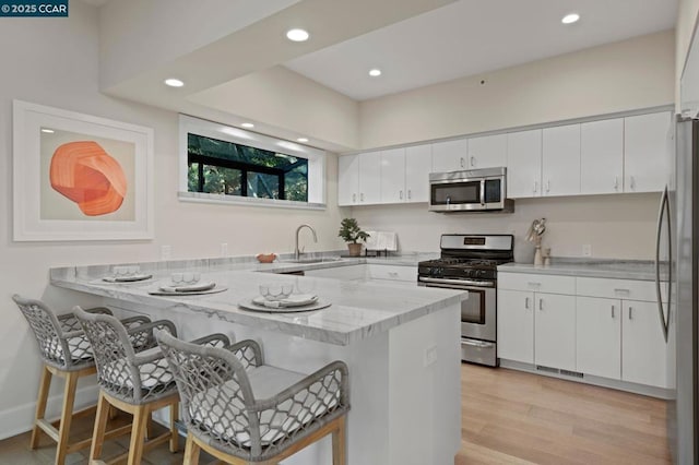 kitchen featuring kitchen peninsula, white cabinets, a breakfast bar, and appliances with stainless steel finishes