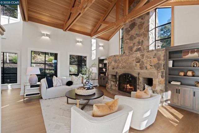 living room with high vaulted ceiling, a wealth of natural light, light hardwood / wood-style floors, and a stone fireplace