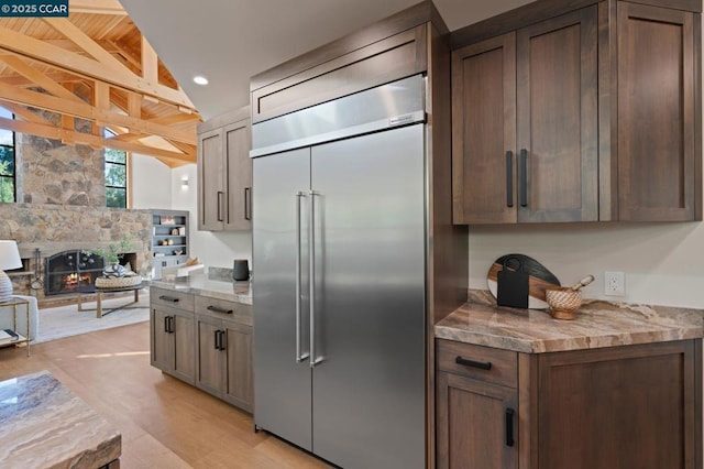 kitchen with built in fridge, light hardwood / wood-style floors, a fireplace, wood ceiling, and vaulted ceiling with beams