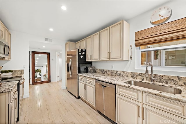 kitchen featuring sink, stainless steel appliances, cream cabinetry, and light stone countertops