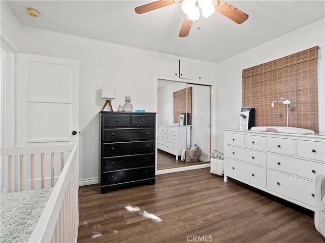 bedroom with ceiling fan, a nursery area, dark hardwood / wood-style floors, and a closet