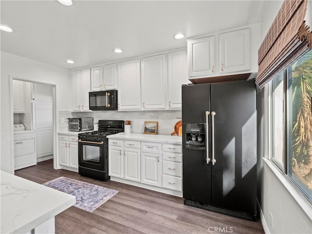 kitchen featuring washer / clothes dryer, white cabinetry, a wealth of natural light, black appliances, and decorative backsplash