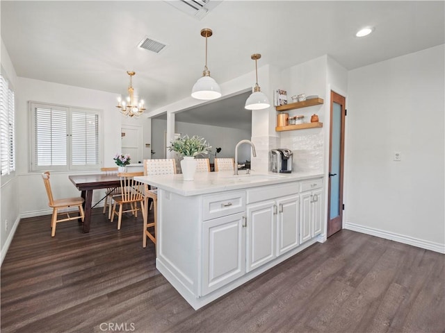 kitchen featuring white cabinetry, sink, kitchen peninsula, pendant lighting, and dark hardwood / wood-style floors