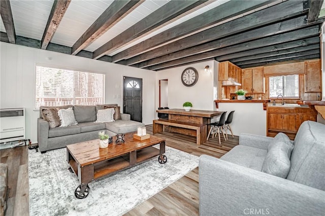 living room featuring beamed ceiling, sink, light hardwood / wood-style flooring, and heating unit