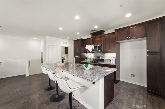 kitchen featuring a kitchen bar, light stone counters, a center island with sink, dark hardwood / wood-style flooring, and stainless steel appliances