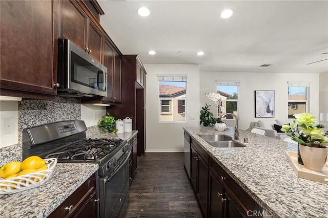 kitchen with appliances with stainless steel finishes, dark hardwood / wood-style floors, sink, backsplash, and light stone countertops