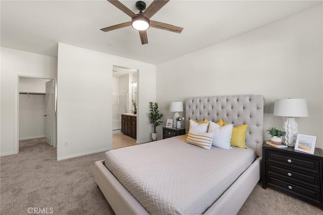 bedroom featuring a spacious closet, ensuite bath, light colored carpet, and ceiling fan