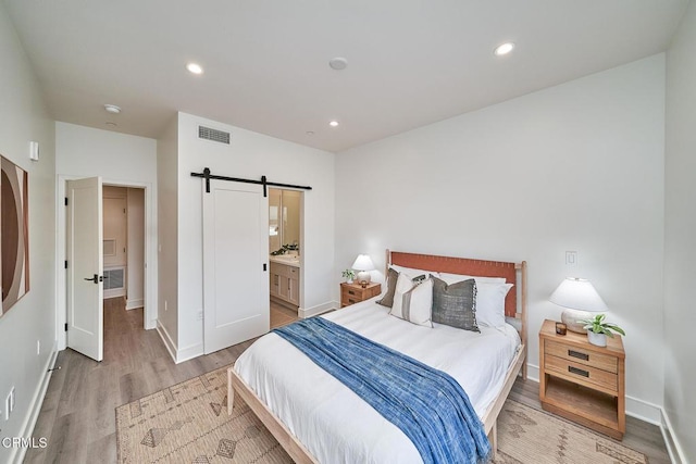 bedroom featuring light wood-type flooring, connected bathroom, and a barn door