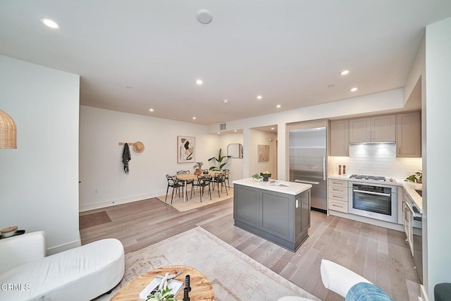 kitchen with appliances with stainless steel finishes, a kitchen island, decorative backsplash, gray cabinets, and light hardwood / wood-style flooring