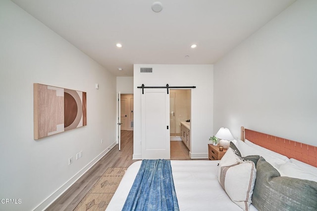 bedroom featuring light wood-type flooring, ensuite bathroom, and a barn door