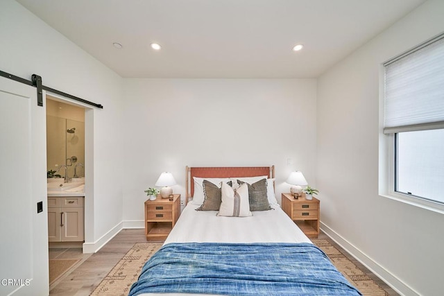 bedroom featuring light hardwood / wood-style flooring, ensuite bathroom, and a barn door