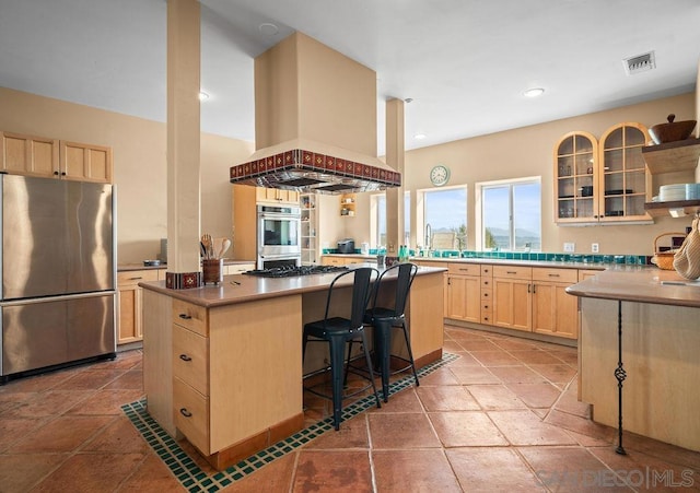 kitchen with a center island, light brown cabinetry, island range hood, stainless steel appliances, and a breakfast bar area