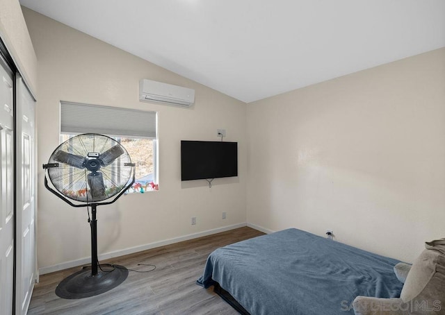 bedroom with a wall mounted air conditioner, light hardwood / wood-style flooring, and vaulted ceiling