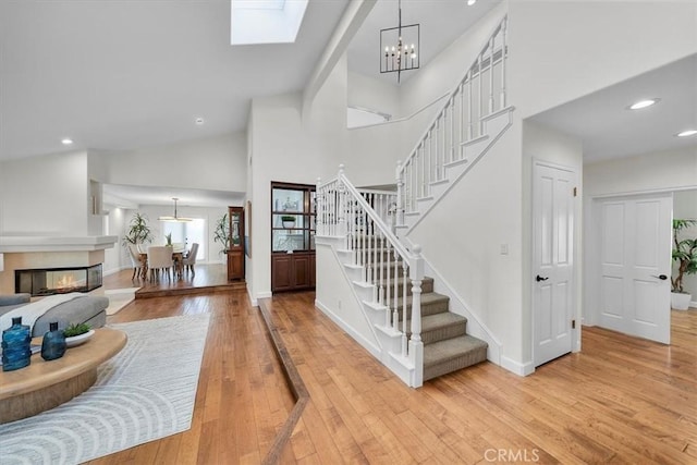 stairway featuring hardwood / wood-style floors, an inviting chandelier, high vaulted ceiling, and a skylight