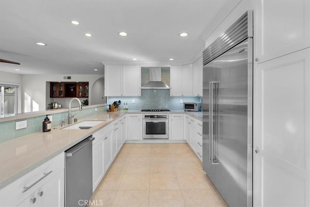 kitchen featuring appliances with stainless steel finishes, wall chimney exhaust hood, sink, backsplash, and white cabinets