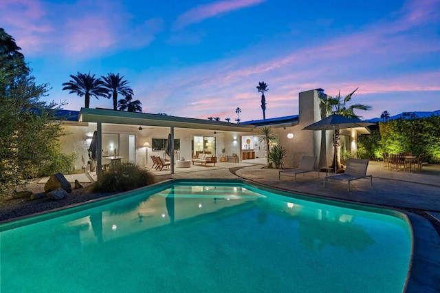 pool at dusk with ceiling fan, a patio area, and outdoor lounge area