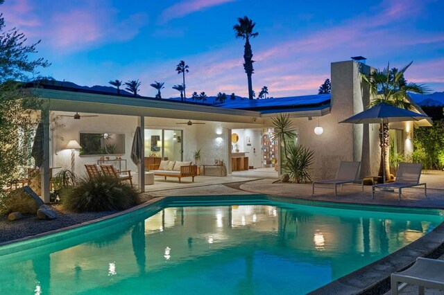 pool at dusk featuring a patio, outdoor lounge area, and ceiling fan