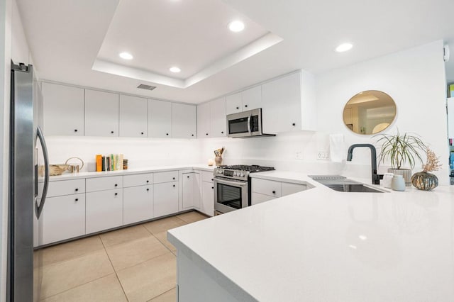 kitchen with appliances with stainless steel finishes, white cabinetry, sink, kitchen peninsula, and a raised ceiling