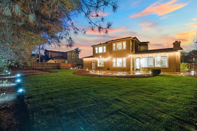 back house at dusk with a lawn and a patio