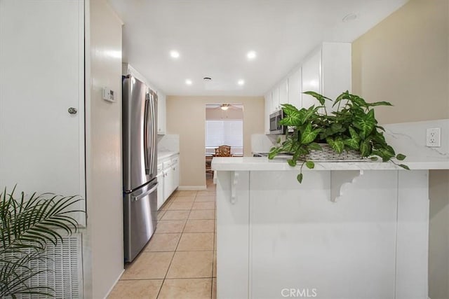 kitchen featuring a breakfast bar, stainless steel appliances, white cabinets, light tile patterned flooring, and kitchen peninsula