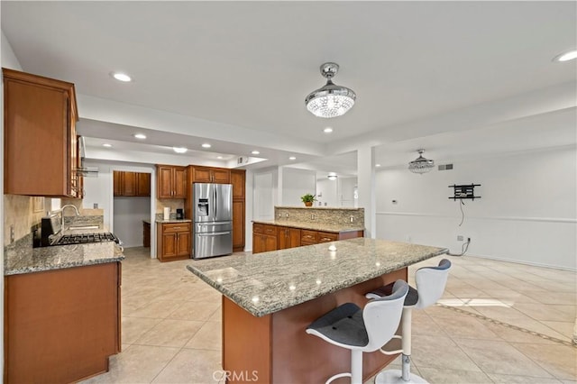 kitchen with tasteful backsplash, stainless steel fridge with ice dispenser, light stone countertops, light tile patterned flooring, and a kitchen island