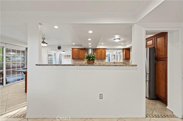 kitchen with light stone countertops, stainless steel refrigerator, kitchen peninsula, and light tile patterned floors