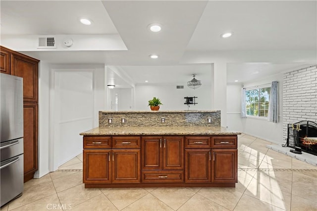 kitchen featuring light tile patterned flooring, light stone counters, decorative backsplash, and stainless steel refrigerator