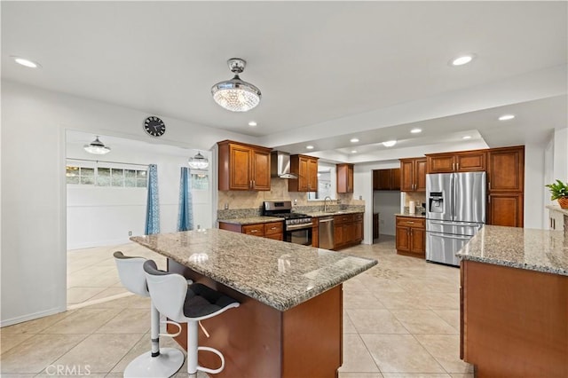 kitchen featuring wall chimney exhaust hood, sink, light stone countertops, a center island, and stainless steel appliances