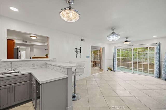 kitchen featuring sink, light tile patterned flooring, kitchen peninsula, and gray cabinets