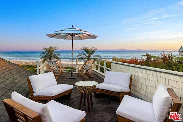 patio terrace at dusk featuring a balcony, a water view, and a view of the beach