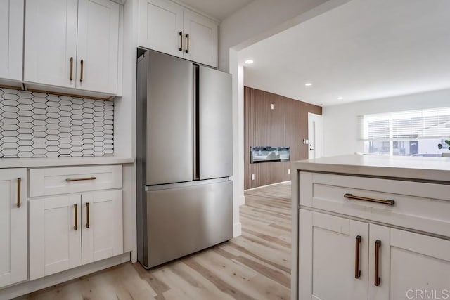 kitchen with white cabinetry, light hardwood / wood-style flooring, tasteful backsplash, and stainless steel refrigerator