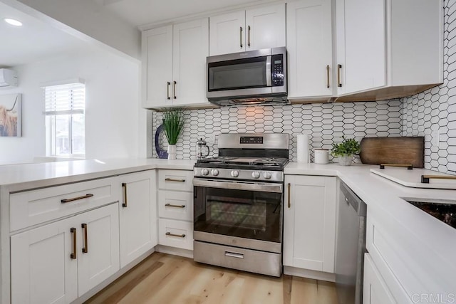 kitchen with an AC wall unit, white cabinets, appliances with stainless steel finishes, decorative backsplash, and light wood-type flooring