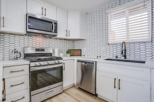 kitchen with white cabinets, appliances with stainless steel finishes, tasteful backsplash, light hardwood / wood-style floors, and sink