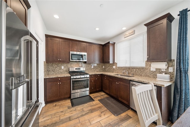 kitchen featuring light stone countertops, appliances with stainless steel finishes, decorative backsplash, dark brown cabinets, and sink