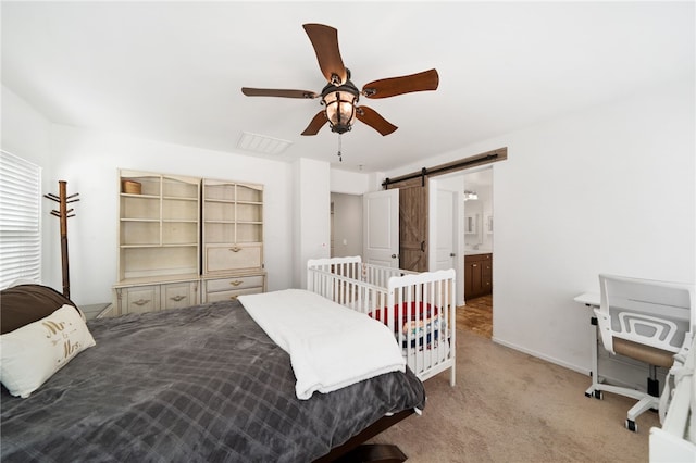 bedroom featuring ceiling fan, ensuite bath, light carpet, and a barn door