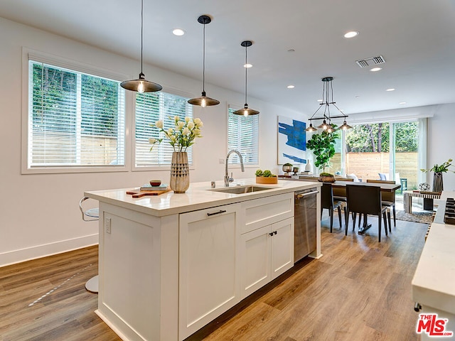 kitchen with hanging light fixtures, stainless steel dishwasher, white cabinets, sink, and a center island with sink