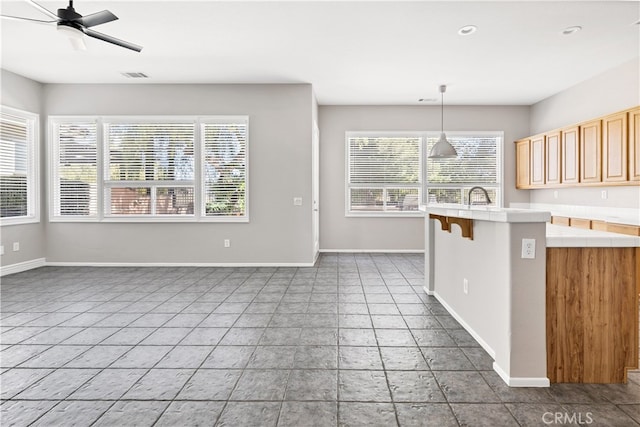 kitchen with a kitchen breakfast bar, light brown cabinets, ceiling fan, hanging light fixtures, and sink