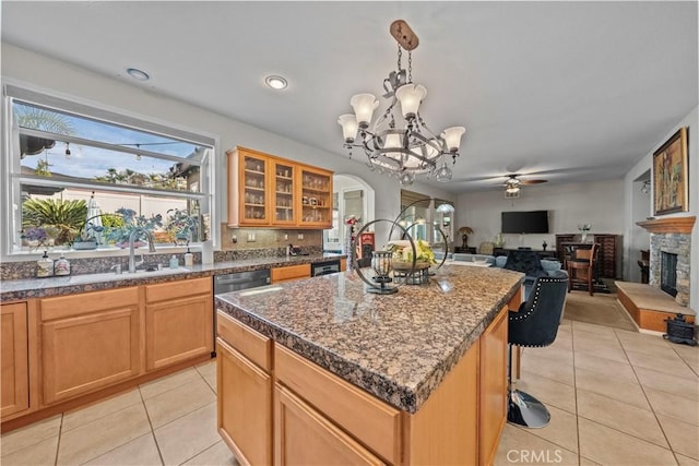 kitchen featuring a kitchen island, a stone fireplace, decorative light fixtures, sink, and light tile patterned floors