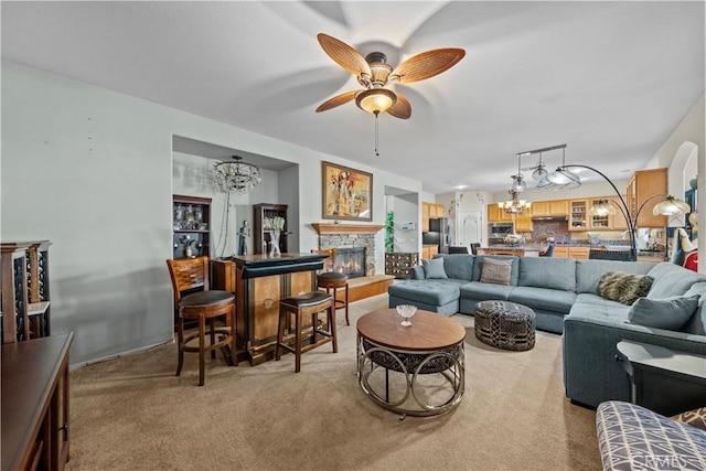 living room featuring light colored carpet, a stone fireplace, and ceiling fan with notable chandelier