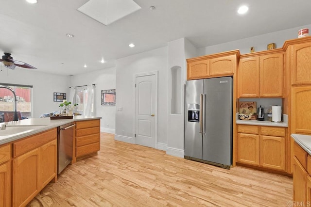 kitchen with a skylight, stainless steel appliances, sink, light wood-type flooring, and ceiling fan