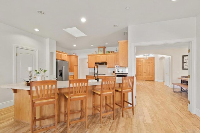 kitchen with light brown cabinets, a kitchen bar, a skylight, light hardwood / wood-style floors, and high end refrigerator