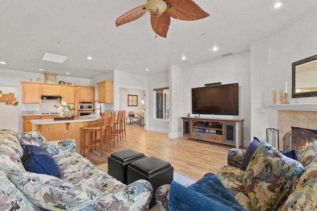 living room featuring sink, a tiled fireplace, light wood-type flooring, and ceiling fan