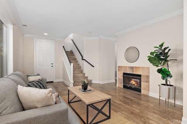 living room with hardwood / wood-style flooring, ornamental molding, and a tiled fireplace